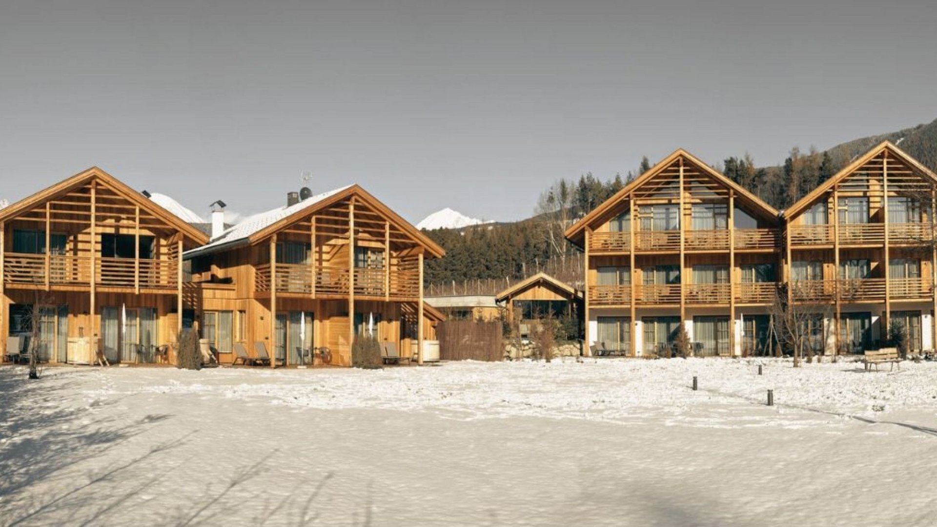 Urlaub in Natz-Schabs? Kessler’s Mountain Lodge! Holzhäuser im Schnee vor bewaldeten Bergen und klarem Himmel