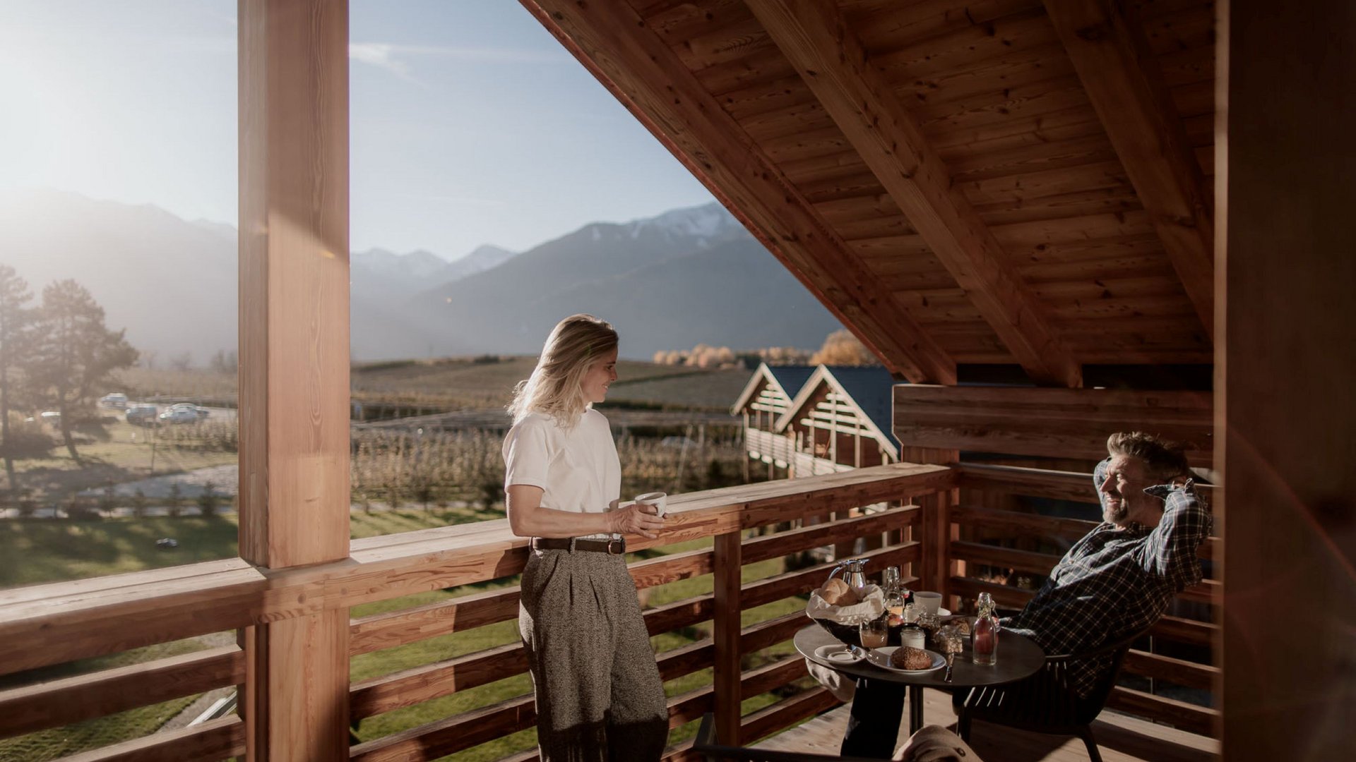 Urlaub in Natz-Schabs? Kessler’s Mountain Lodge! Zwei Personen genießen Kaffee auf einem Balkon mit Bergblick am Morgen
