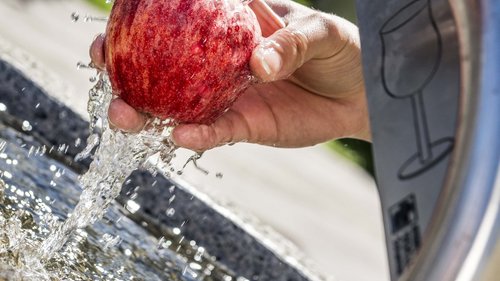 Urlaub in Natz-Schabs? Kessler’s Mountain Lodge! Hand wäscht roten Apfel unter fließendem Wasser aus Trinkbrunnen