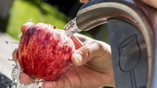 Festa Sotto le Stelle Mano che lava una mela rossa sotto un getto d'acqua potabile