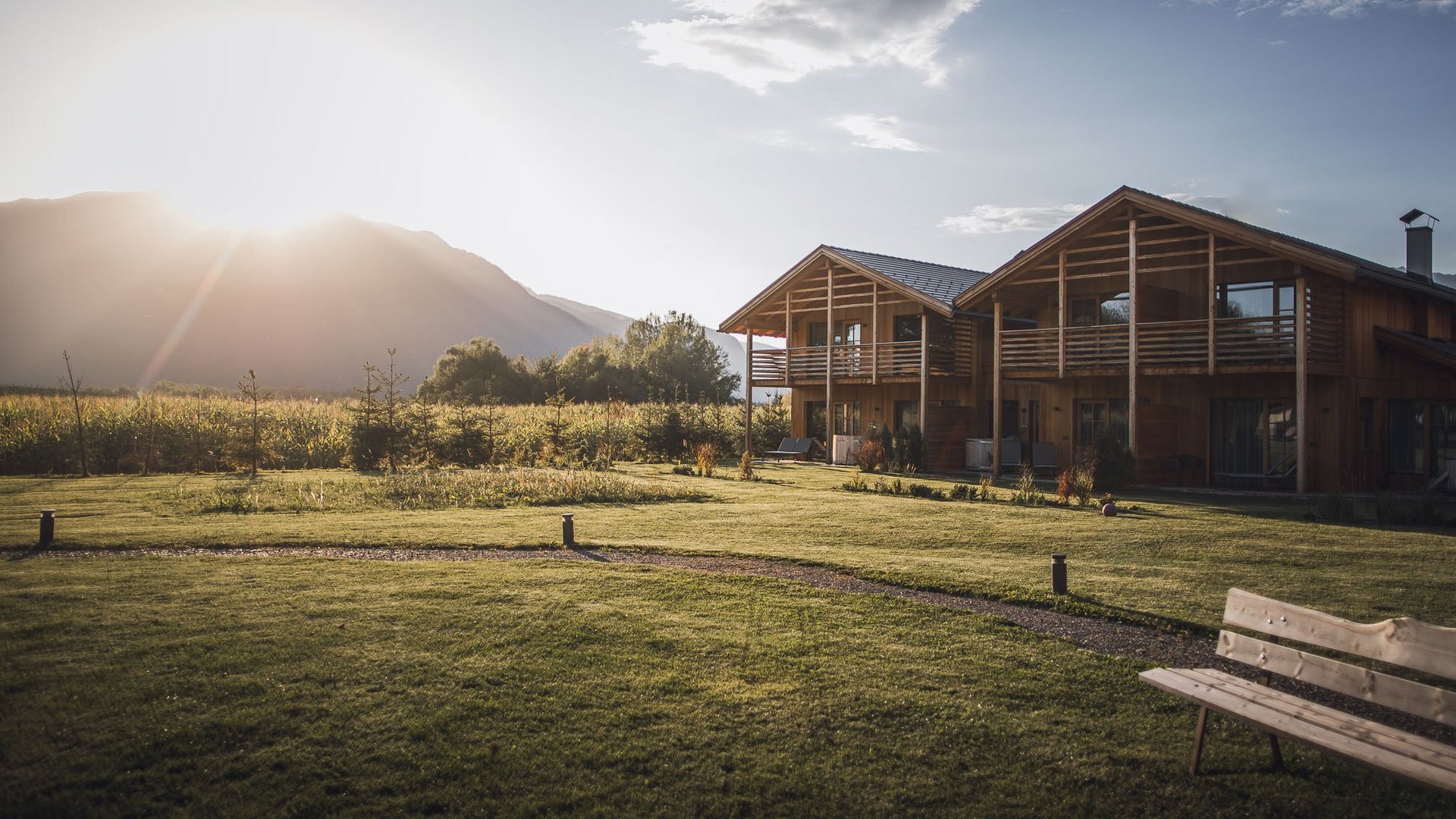 Urlaub in Natz-Schabs? Kessler’s Mountain Lodge! Holzhaus in sonniger Landschaft mit Bergen und Wiese