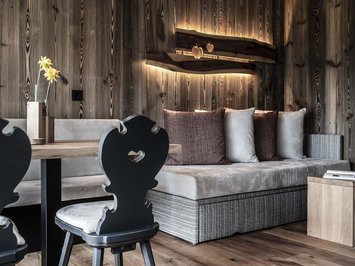 Urlaub in Natz-Schabs? Kessler’s Mountain Lodge! Gemütliche Sitzecke mit Holzwänden, Sofa, Stühlen und dekorativer Wandbeleuchtung