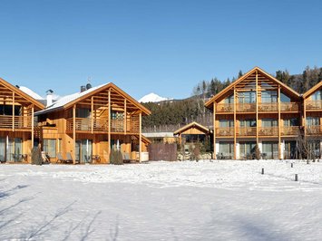 Urlaub in Natz-Schabs? Kessler’s Mountain Lodge! Holzhäuser im Schnee vor Bergkulisse bei klarem Himmel