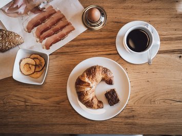 Urlaub in Natz-Schabs? Kessler’s Mountain Lodge! Frühstück mit Croissant, Kaffee, Ei, Schinken und Trockenfrüchten auf Holztisch
