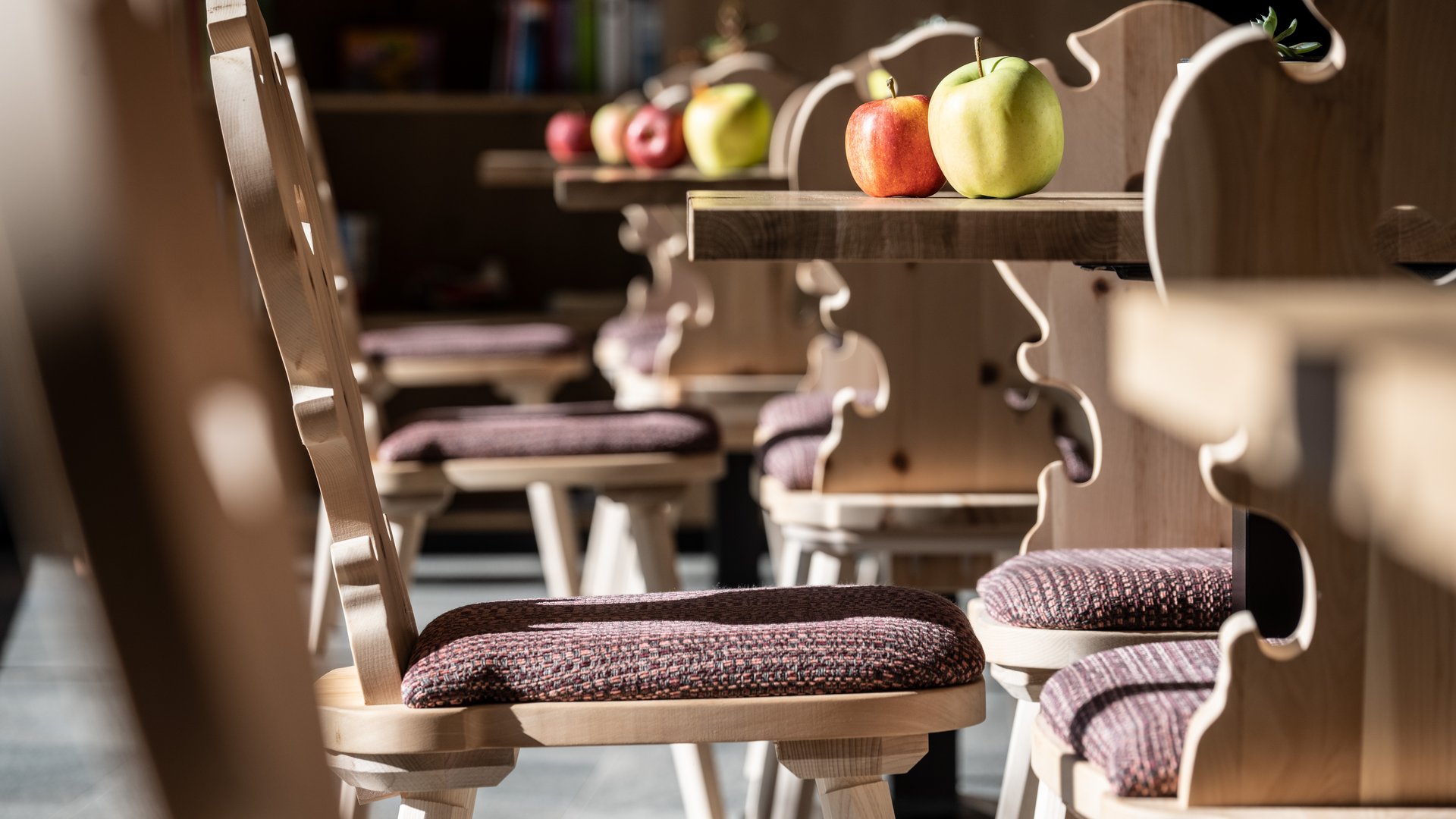 Alpine chalet in South Tyrol with a farm shop Wooden chairs with cushions and apples on wooden tables in a bright room