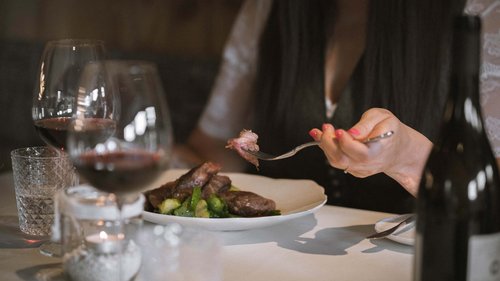 Urlaub in Natz-Schabs? Kessler’s Mountain Lodge! Person isst Steak mit Rosenkohl in elegantem Restaurant mit Rotwein.