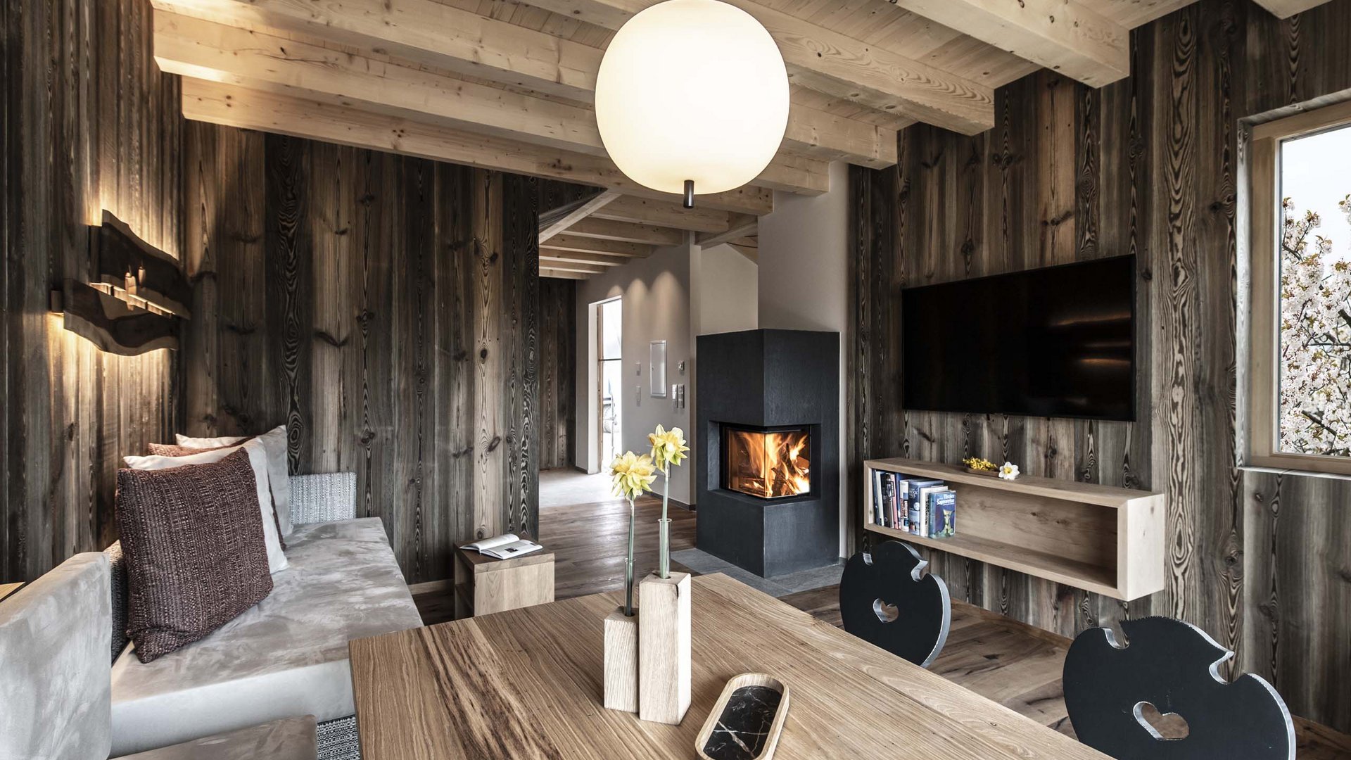 Urlaub in Natz-Schabs? Kessler’s Mountain Lodge! Gemütliches Wohnzimmer mit Holzverkleidung, Kamin und modernem Fernseher