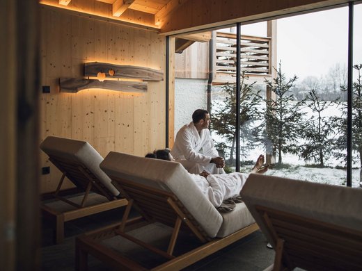 Urlaub in Natz-Schabs? Kessler’s Mountain Lodge! Zwei Personen in Bademänteln entspannen auf Liegen mit Blick auf verschneite Landschaft