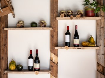 Alpine chalet in South Tyrol with a farm shop Wooden shelves with wine bottles, jam jars, and gourds on white wall