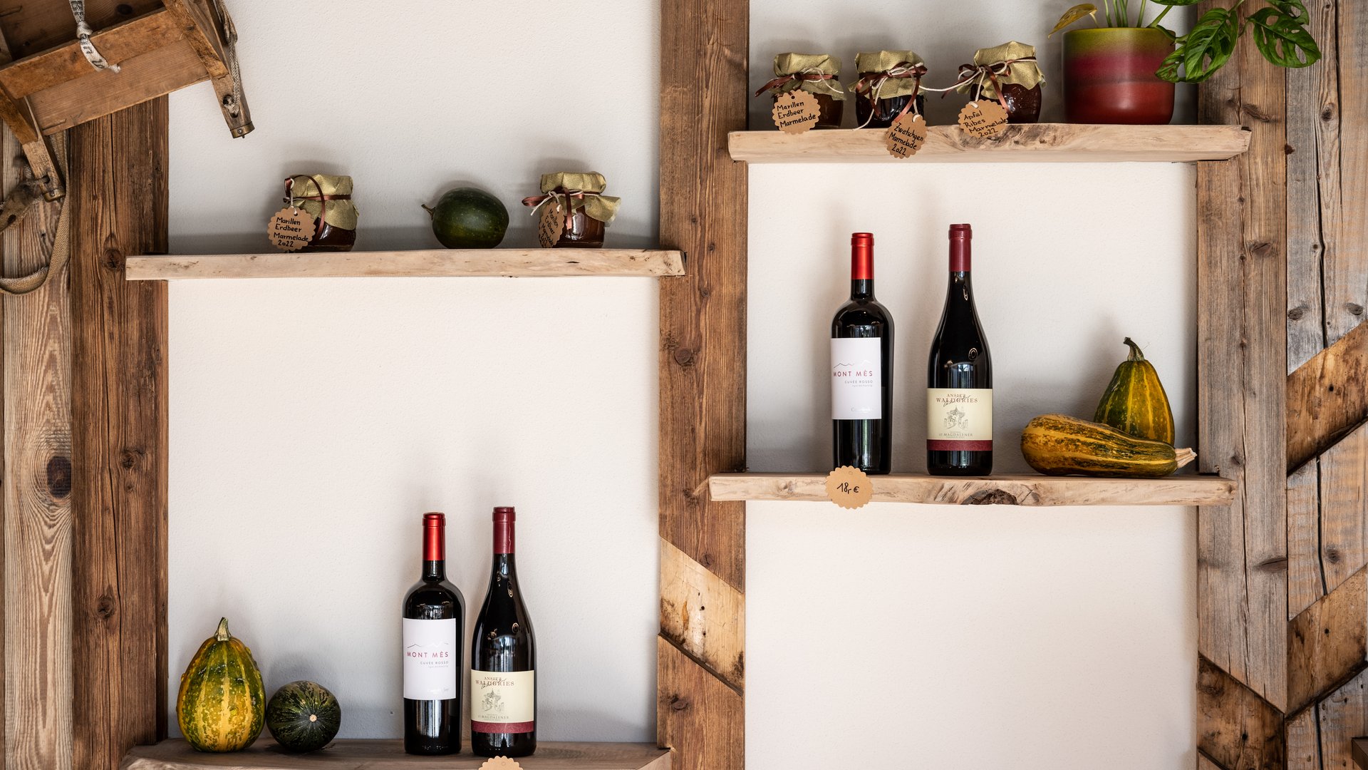 Alpine chalet in South Tyrol with a farm shop Wooden shelves with wine bottles, jam jars, and gourds on white wall