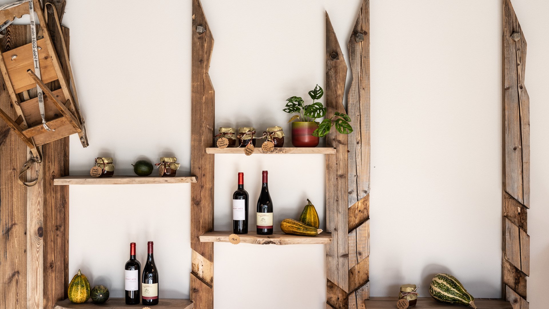 Alpine chalet in South Tyrol with a farm shop Rustic wooden shelf with wine bottles, jams, gourds, and a plant