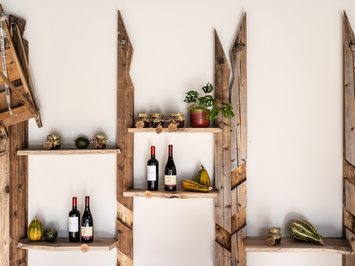 Alpine chalet in South Tyrol with a farm shop Rustic wooden shelf with wine bottles, jams, gourds, and a plant