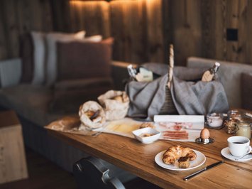 Urlaub in Natz-Schabs? Kessler’s Mountain Lodge! Gemütliches Frühstück mit Croissant, Kaffee und verschiedenen Aufstrichen auf Holztisch